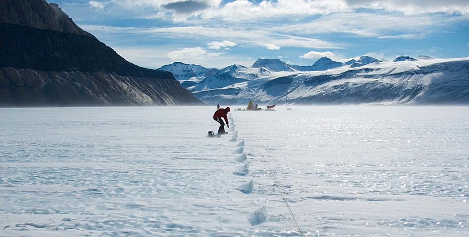 Teammitglied Daniel Baggenstoss nimmt Proben aus dem Eis. Im Hintergrund steht das Forschungscamp. Â© Hinrich Schaefer